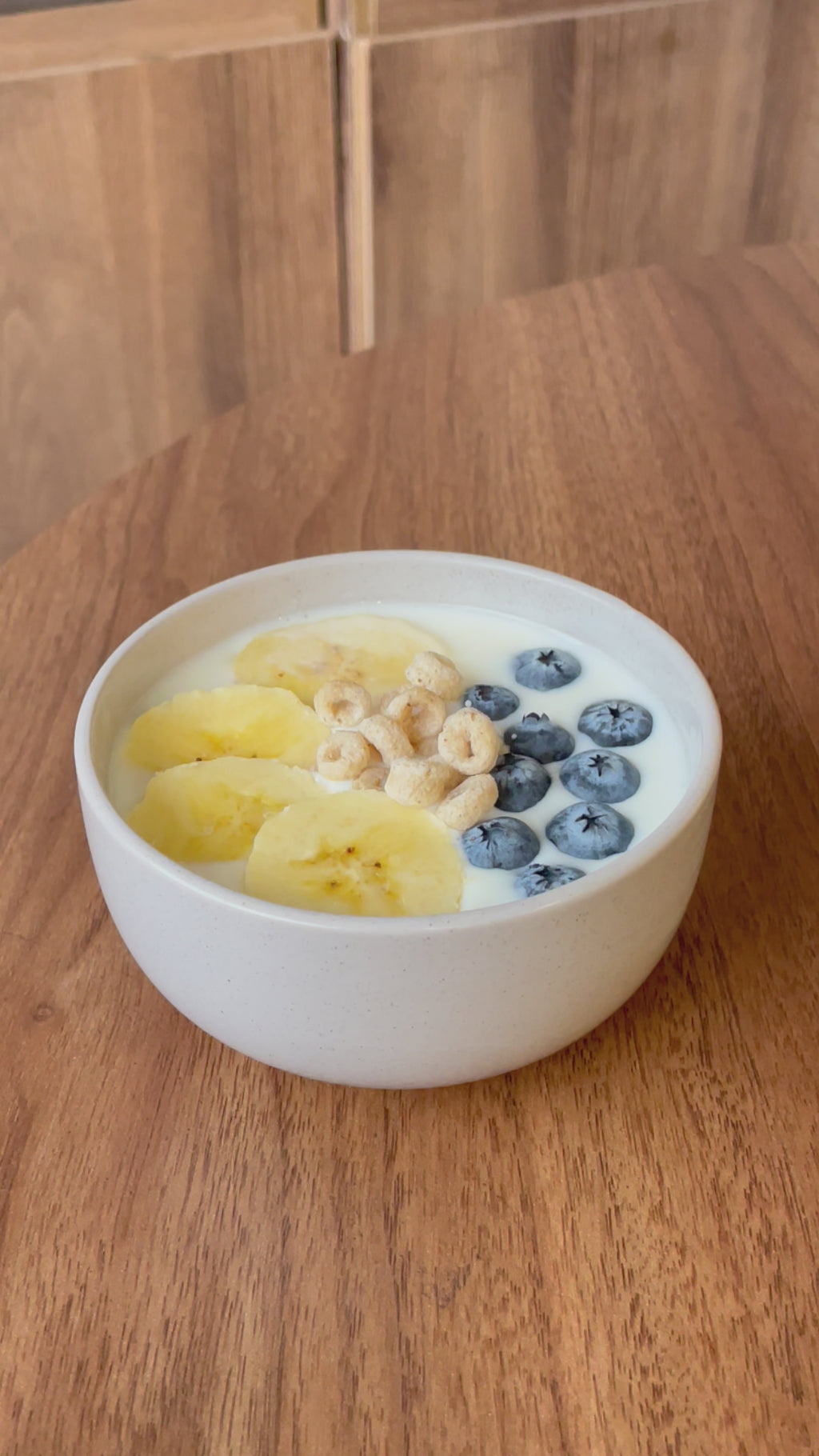 Elari in bowl of milk with bananas and strawberries and the loop shaped cereal drop from out of frame